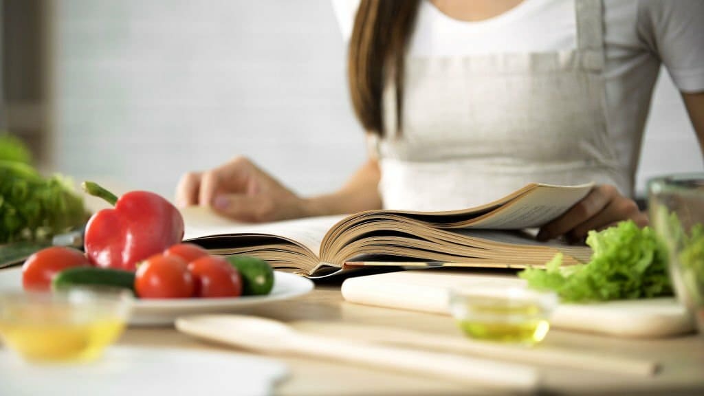 Lecture de livre de cuisine avec des légumes frais et des ustensiles de cuisine sur la table